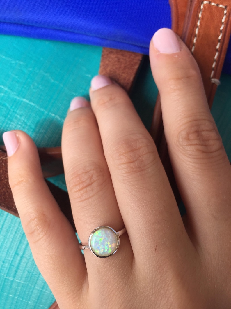 May include: A silver ring with a white opal gemstone. The ring is on a person's finger.