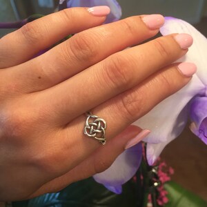 May include: A silver Celtic knot ring on a finger with pink nail polish. The ring is a simple design with a knot in the center.