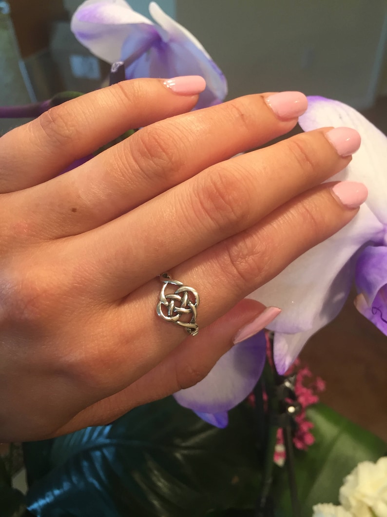 May include: A silver Celtic knot ring on a finger with pink nail polish. The ring is a simple design with a knot in the center.