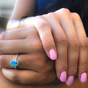 May include: A silver ring with a blue oval opal gemstone surrounded by a halo of smaller stones.