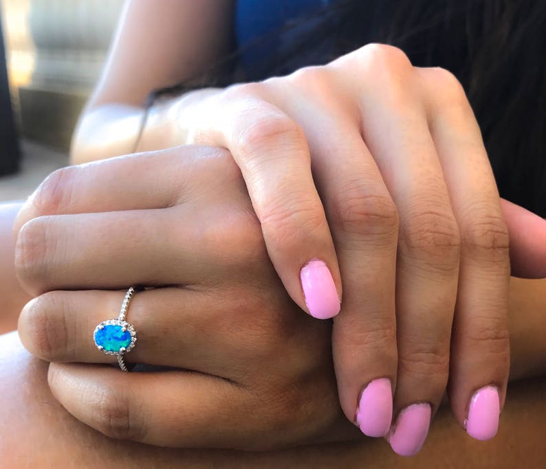 May include: A silver ring with a blue oval opal gemstone surrounded by a halo of smaller stones.
