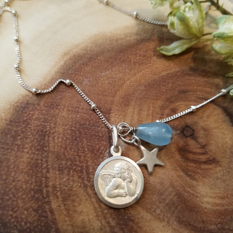 May include: A silver chain necklace with a charm featuring a sleeping angel, a star, and a light blue gemstone.