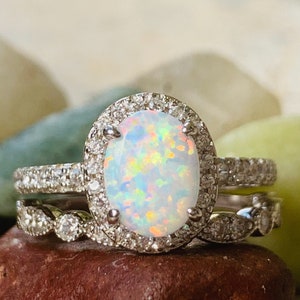 May include: A silver ring set with a large oval opal surrounded by a halo of smaller diamonds. The ring is set on a brown stone.