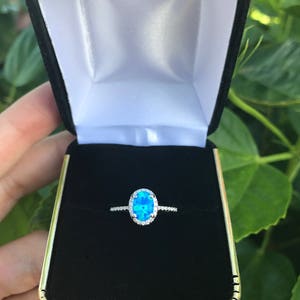May include: A silver ring with a blue oval opal gemstone surrounded by a halo of smaller diamonds.