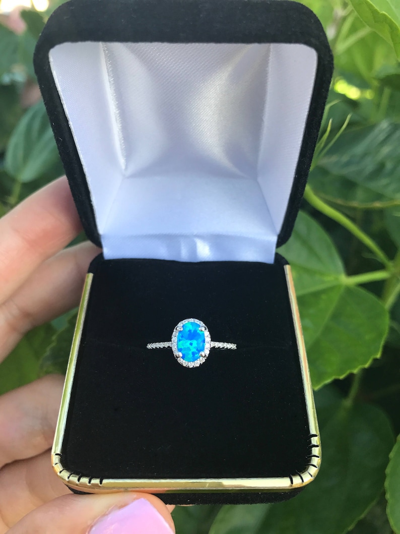 May include: A silver ring with a blue oval opal gemstone surrounded by a halo of smaller diamonds.