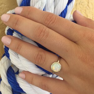 May include: A gold ring with a white opal gemstone. The ring is on a finger of a hand.