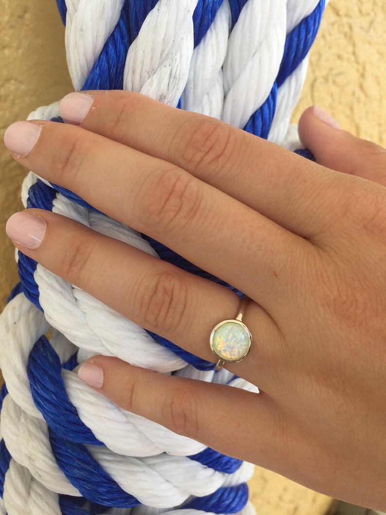 May include: A gold ring with a white opal gemstone. The ring is on a finger of a hand.
