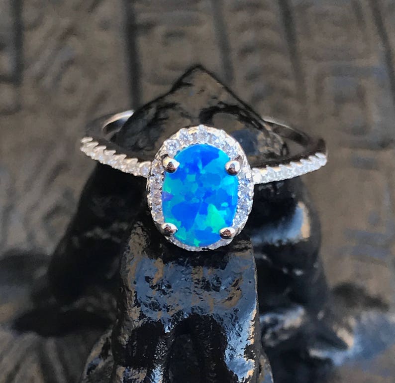 May include: A silver ring with a blue opal gemstone surrounded by a halo of smaller clear stones.
