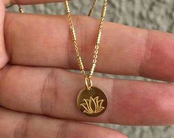 May include: A gold chain necklace with a small round pendant featuring a lotus flower design.