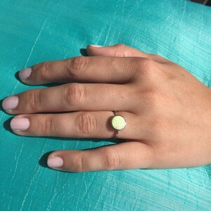 May include: A silver ring with a white opal gemstone. The ring is on a person's finger.
