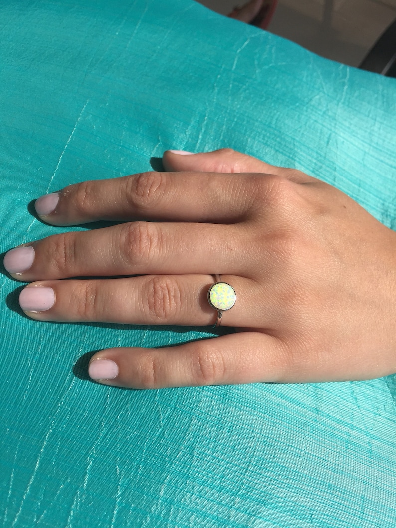 May include: A silver ring with a white opal gemstone. The ring is on a person's finger.