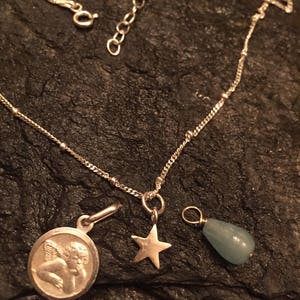 May include: A silver chain necklace with three charms: a cherub, a star, and a teardrop-shaped aquamarine stone.
