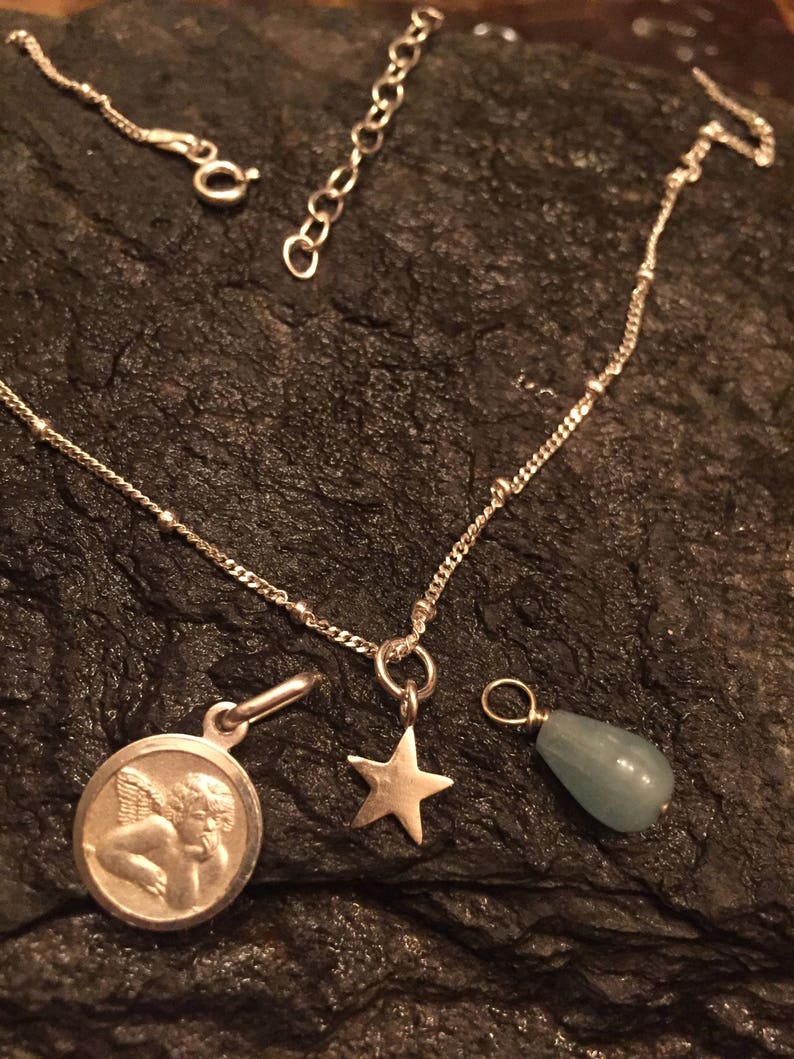 May include: A silver chain necklace with three charms: a cherub, a star, and a teardrop-shaped aquamarine stone.