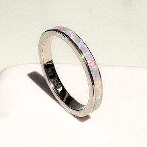 May include: A silver ring featuring an inlaid opal band. The opal displays a blend of pink, white, and iridescent hues. The ring is presented against a white backdrop, emphasizing its design and details.
