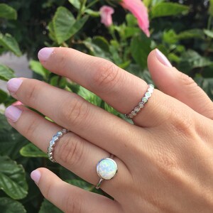 May include: Two silver rings on a hand. The top ring has a white opal stone. The bottom ring is a band of small silver circles.