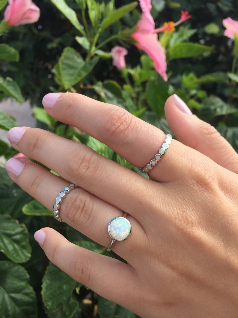 May include: Two silver rings on a hand. The top ring has a white opal stone. The bottom ring is a band of small silver circles.