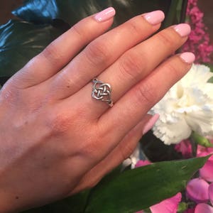 May include: A silver Celtic knot ring with a simple design. The ring is worn on a hand with pink nail polish.