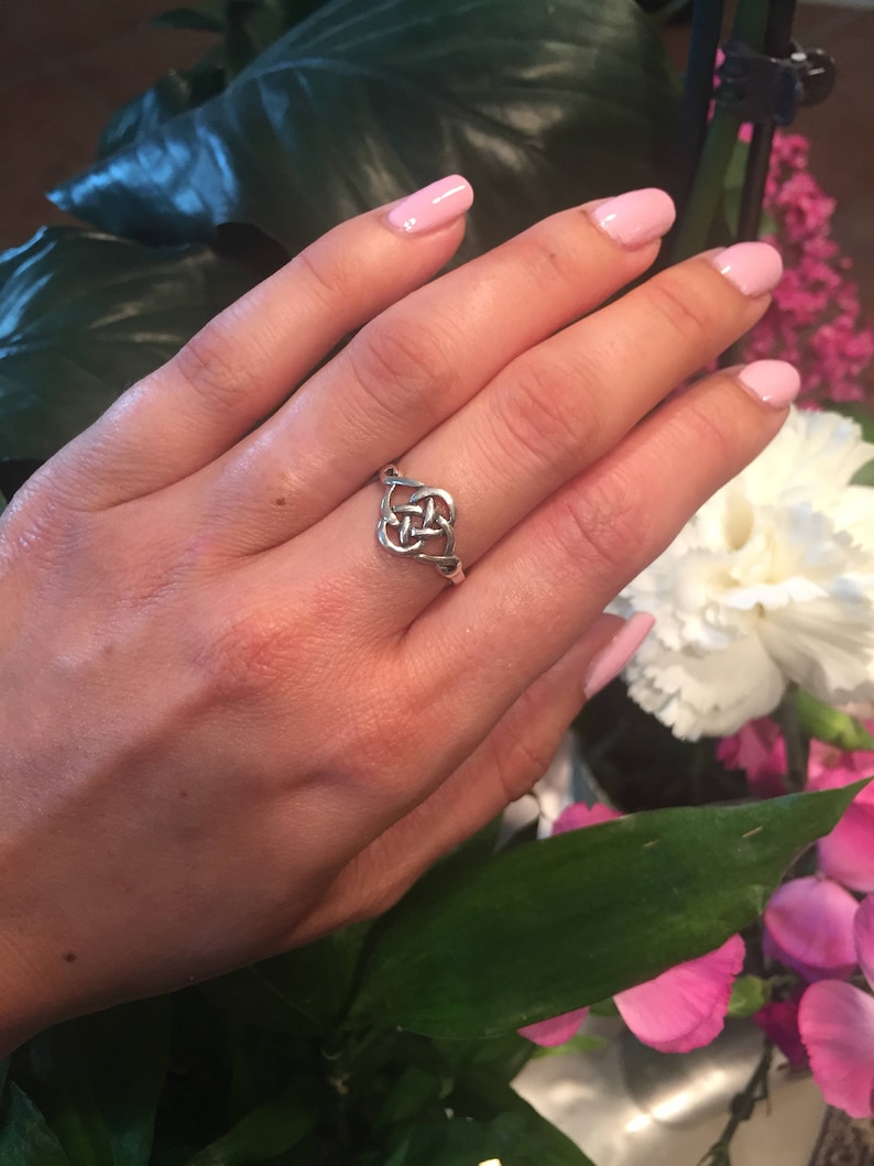 May include: A silver Celtic knot ring with a simple design. The ring is worn on a hand with pink nail polish.