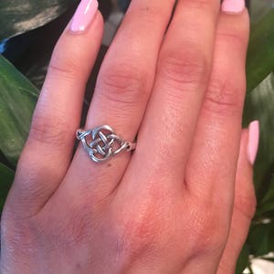 May include: A silver Celtic knot ring with a simple design. The ring is worn on the ring finger of a hand with pink nail polish.