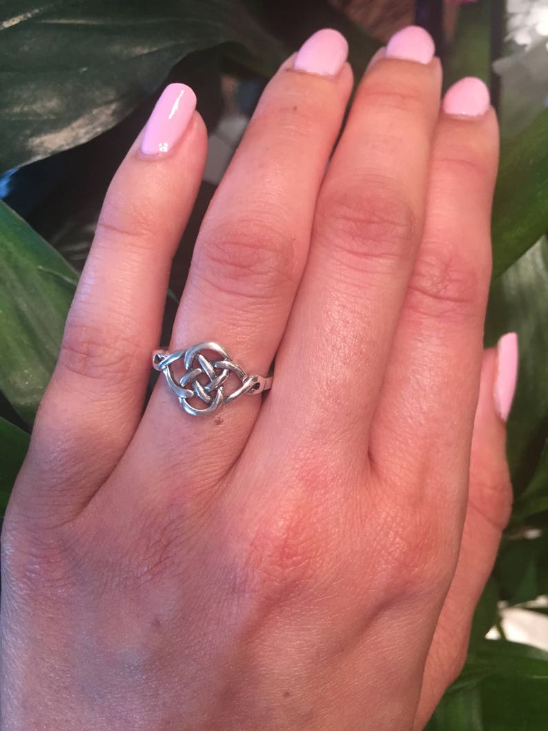 May include: A silver Celtic knot ring with a simple design. The ring is worn on the ring finger of a hand with pink nail polish.