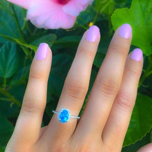 May include: A silver ring with a blue oval gemstone surrounded by smaller clear gemstones.