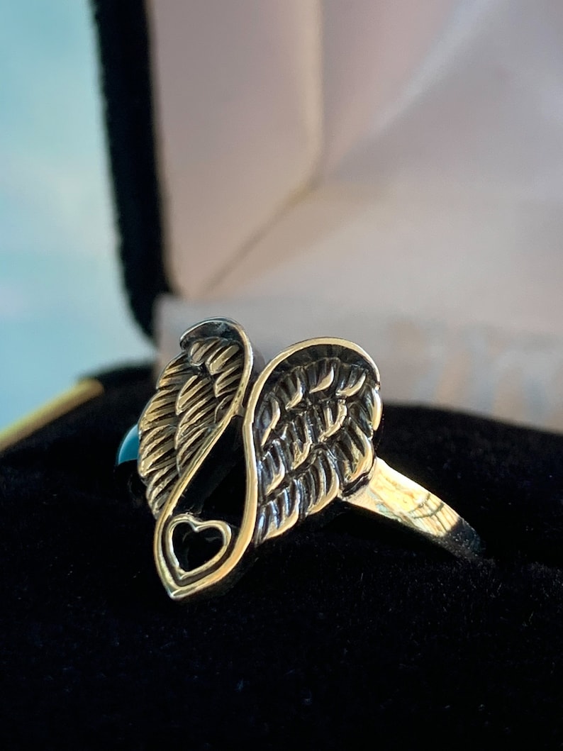 Peut inclure: Une bague dor&eacute;e avec un motif d'ailes d'ange. La bague pr&eacute;sente des textures de plumes d&eacute;taill&eacute;es et une d&eacute;coupe en forme de c&oelig;ur. La bague est pr&eacute;sent&eacute;e dans un &eacute;crin en velours noir.