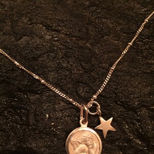 May include: A silver necklace with a round pendant featuring a sleeping angel and a small star charm.