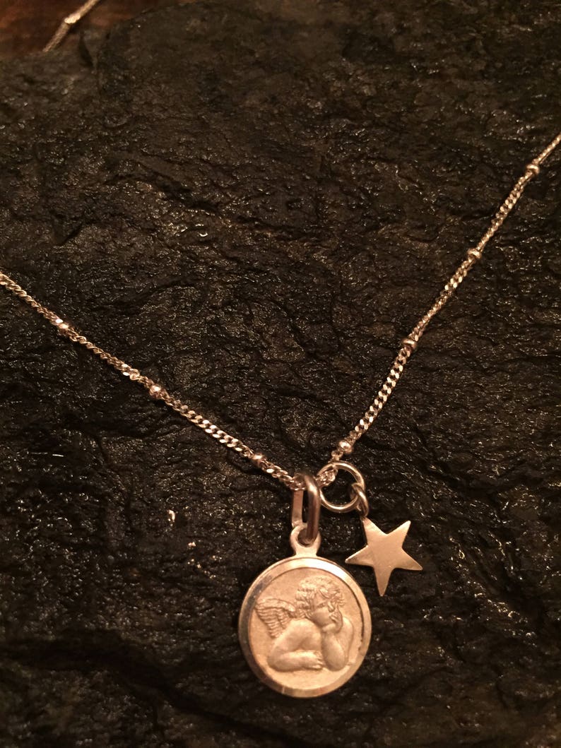 May include: A silver necklace with a round pendant featuring a sleeping angel and a small star charm.