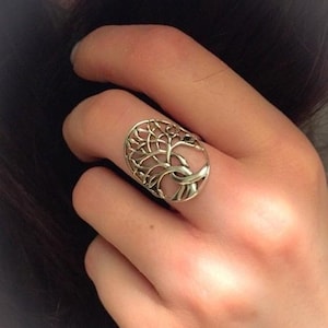 May include: A silver ring with a tree of life design. The ring is open and has a delicate, intricate design.