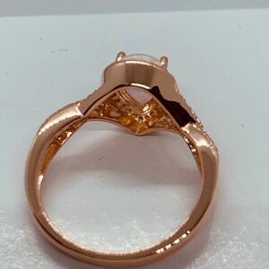 Op de afbeelding: Ros&eacute;gouden ring met een peervormige opaal middensteen. De band heeft een gedraaid ontwerp met kleine, heldere accentstenen. De ring staat tegen een witte achtergrond, waardoor de details van het sieraad worden benadrukt.