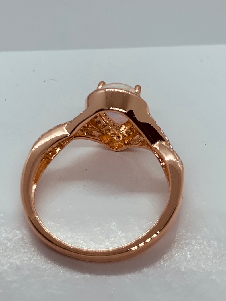 Op de afbeelding: Ros&eacute;gouden ring met een peervormige opaal middensteen. De band heeft een gedraaid ontwerp met kleine, heldere accentstenen. De ring staat tegen een witte achtergrond, waardoor de details van het sieraad worden benadrukt.