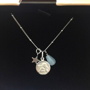 May include: A silver necklace with a charm of an angel, a star, and a light blue teardrop-shaped stone.