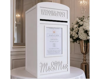 Puede incluir: Una caja de correo de boda de madera blanca con las palabras "WEDDING POST" recortadas en la parte superior. La caja tiene una ranura para tarjetas y un letrero enmarcado con los nombres "Sarah & Adam". Las palabras "Mr & Mrs" están recortadas en la parte inferior.