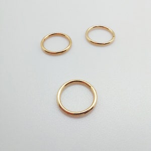 Puede incluir: Tres pendientes de aro circulares de color dorado. Los pendientes est&aacute;n hechos de un metal liso y brillante y son de diferentes tama&ntilde;os. Los aros se muestran sobre una superficie blanca.