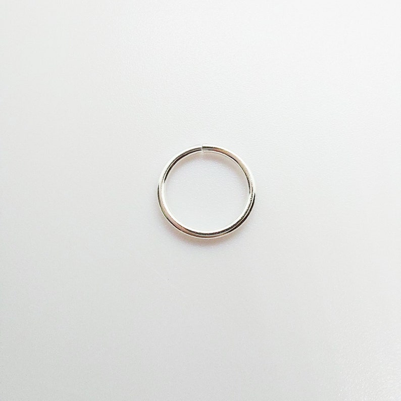 May include: A small, silver-colored ring with a circular design. The ring is made of a shiny metal and is set against a plain white background. The ring's diameter appears to be approximately 0.5 inches.
