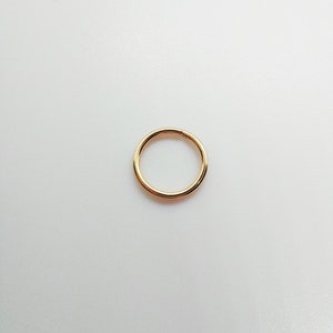 May include: A simple, circular gold-toned hoop ring with a smooth, polished finish. The ring features a seamless design with a single visible join line, creating a continuous, minimalist circular shape that is uniform in thickness throughout.