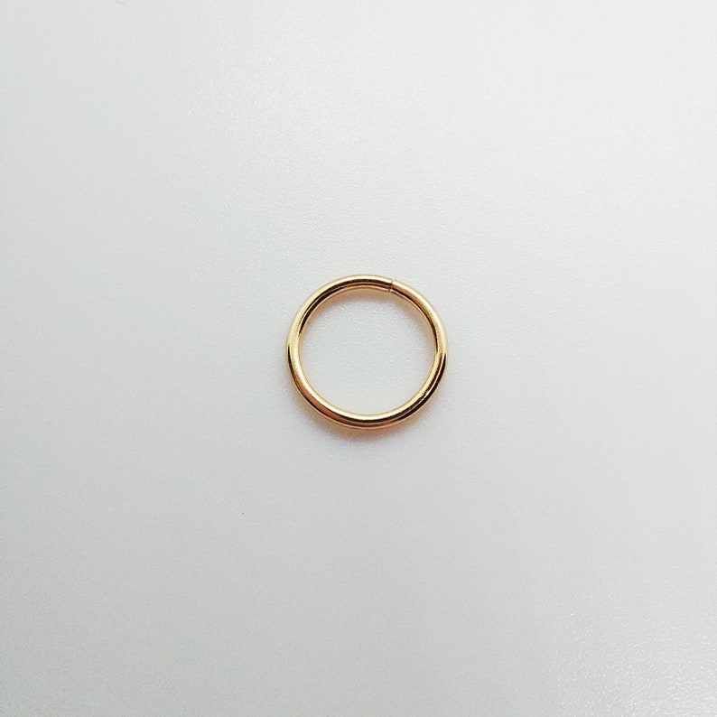 May include: A simple, circular gold-toned hoop ring with a smooth, polished finish. The ring features a seamless design with a single visible join line, creating a continuous, minimalist circular shape that is uniform in thickness throughout.