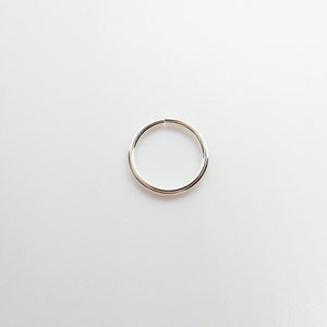 May include: A simple, thin, circular silver-colored hoop ring. The metal band has a smooth, polished finish and features a single, clean break where the two ends meet, allowing the hoop to be opened and closed for insertion or adjustment.