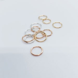 Puede incluir: Una colecci&oacute;n de peque&ntilde;os y finos pendientes de aro en varios acabados met&aacute;licos, incluyendo oro, plata y oro rosa. Los pendientes est&aacute;n dispersos sobre una superficie blanca, mostrando su dise&ntilde;o circular y sencillo. Adecuados para el uso diario.