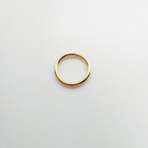 May include: A single, gold-colored, circular earring or nose ring. The jewelry is a simple, seamless ring design, with a smooth, polished surface. The ring is set against a plain white background.