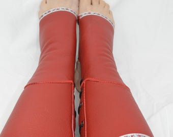 Peut inclure: Jambières en cuir rouge avec une bordure décorative argentée et blanche. Les jambières sont lacées sur le côté avec des lacets noirs. La personne porte un jean bleu.