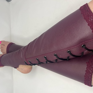May include: Burgundy leg warmers with lace trim at the top and bottom. The leg warmers have a faux leather appearance and black lacing up the side. The foot area is open.