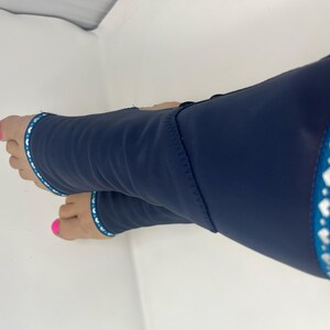 May include: Navy blue compression sleeves with a white and teal heart-patterned trim. The sleeves cover the foot and lower leg. The person's toes are visible, painted with bright pink nail polish.