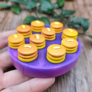 Può includere: Uno stampo in silicone viola con 10 stampi in miniatura a forma di pancake. Gli stampi sono riempiti con argilla polimerica gialla e marrone, che assomigliano a pancake in miniatura.