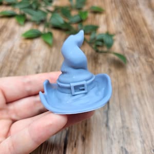 Könnte beinhalten: Ein blauer Hexenhut mit einer spitzen Spitze und einer schwarzen Schnalle. Der Hut ist aus einem glatten, weichen Material gefertigt.