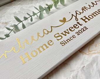 May include: White wooden sign with gold lettering that reads "Welcome Home Sweet Home since 2022" with a gold heart above the word "Home".