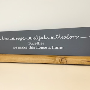Puede incluir: Un letrero de madera gris con texto blanco que dice "tim ♥ roya ♥ elijah ♥ theodore Juntos hacemos de esta casa un hogar".