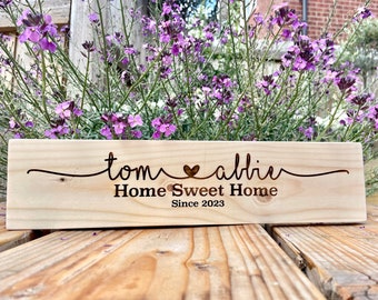 May include: A wooden sign with the text "tom ♥ albie Home Sweet Home Since 2023" engraved on it. The sign is light brown and has a natural wood grain.