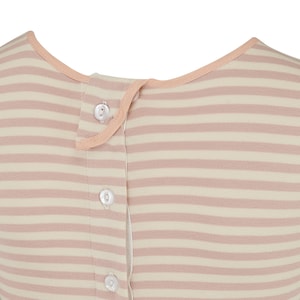 May include: Close-up of a striped garment in cream and pale pink. The fabric features horizontal stripes and a row of white buttons down the front. The neckline and button placket are trimmed with a soft peach-colored fabric.