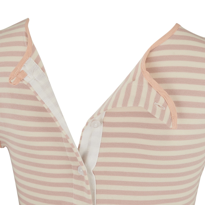 May include: Close-up of a striped top in a soft pink and cream color palette. The top features a button-down design with a contrasting white inner lining and a delicate pink trim along the collar and edges. The fabric has a horizontal striped pattern.